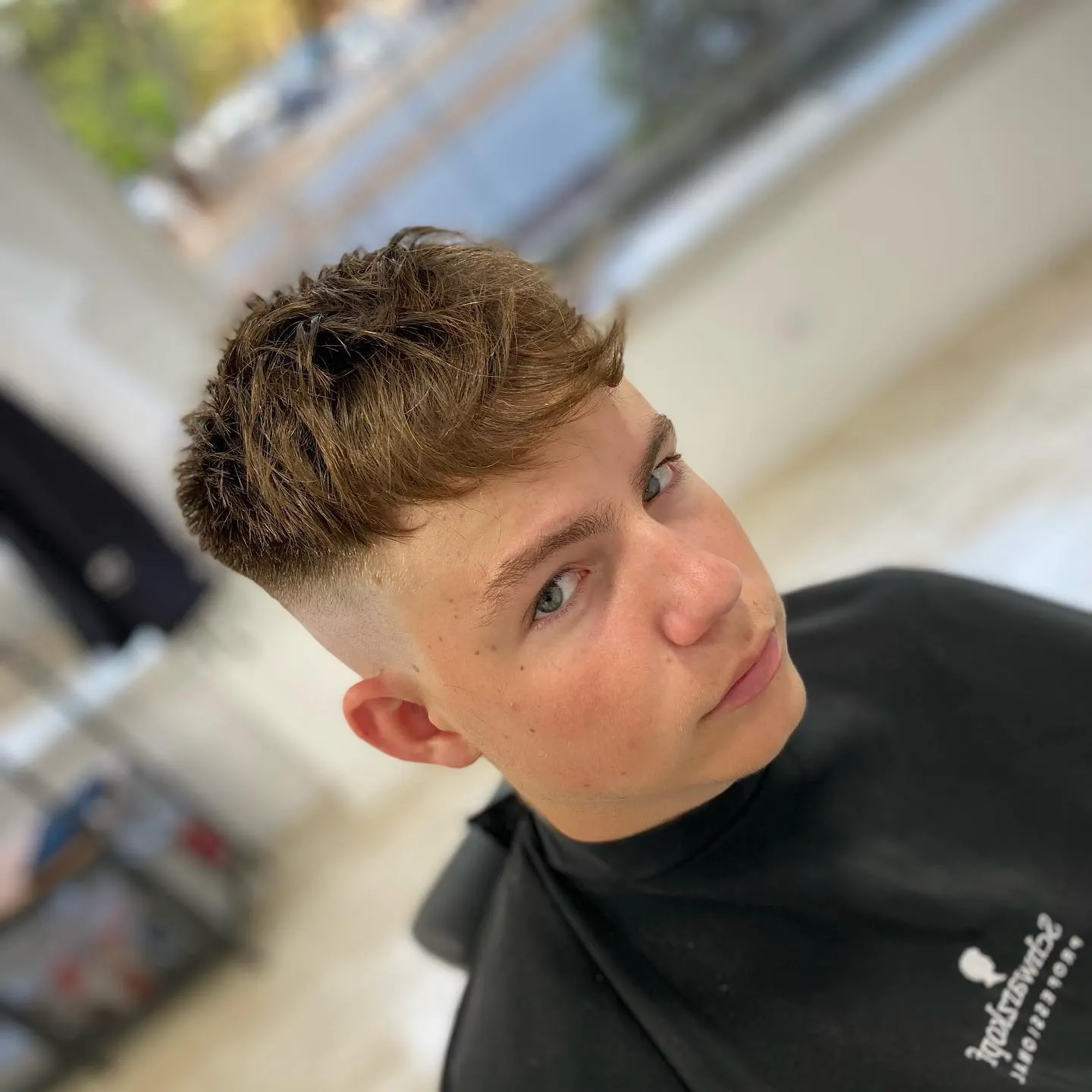 Joven con corte de cabello moderno, mostrando un estilo con textura en la parte superior y desvanecido en los lados, en un ambiente de barbería.