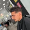 Hombre con corte de cabello moderno y desvanecido, sentado en una barbería, con un enfoque en el estilo y la atención al detalle. Fondo desenfocado que muestra el ambiente del salón.